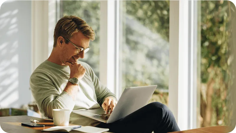 Guy smiling while on a laptop next to a coffee mug
